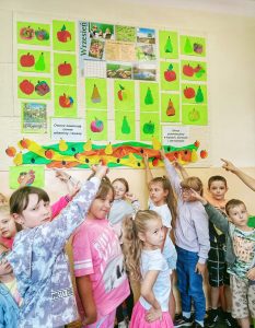 Grupa dzieci stojąca pod gazetka z pracami o owocach